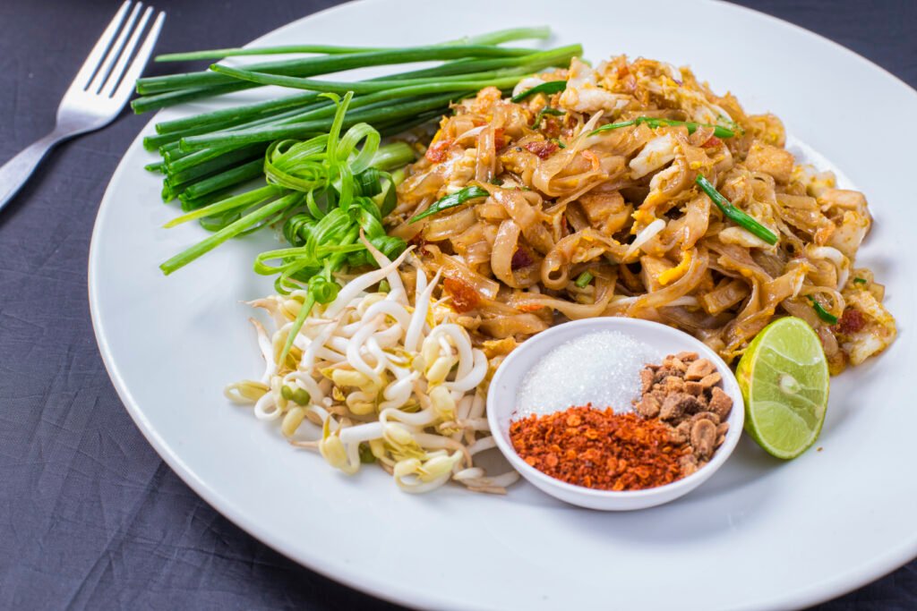 Authentic Pad Thai noodles with lime, chili flakes, bean sprouts, and green onions on a white plate served at Fullmoon Thai Kitchen